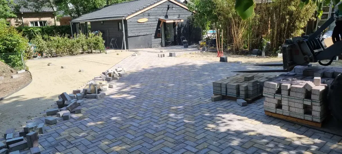 Betonklinkers in keperverband op een oprit, met pallets stenen en een zichtbare straatlaag van zand