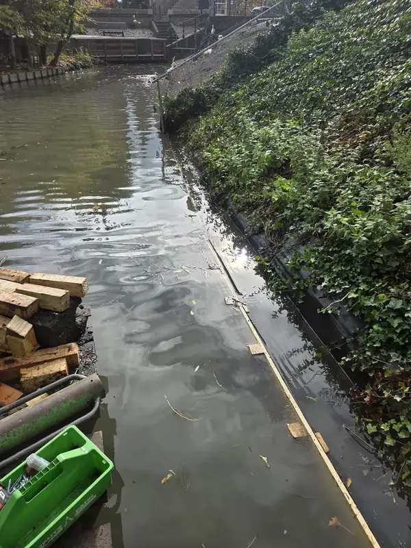 Vervanging van een beschoeiing langs een stadswatergang, met hardhouten planken op een werkboot